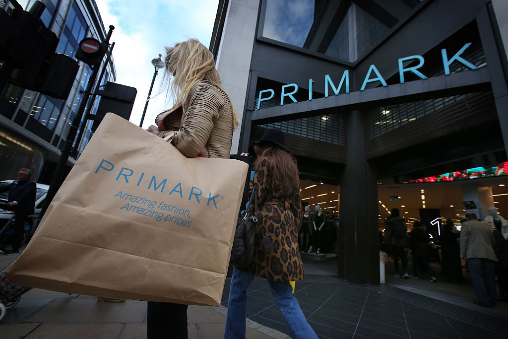 A woman leaves a Primark store with her child, carry a paper Primark bag with her purchases